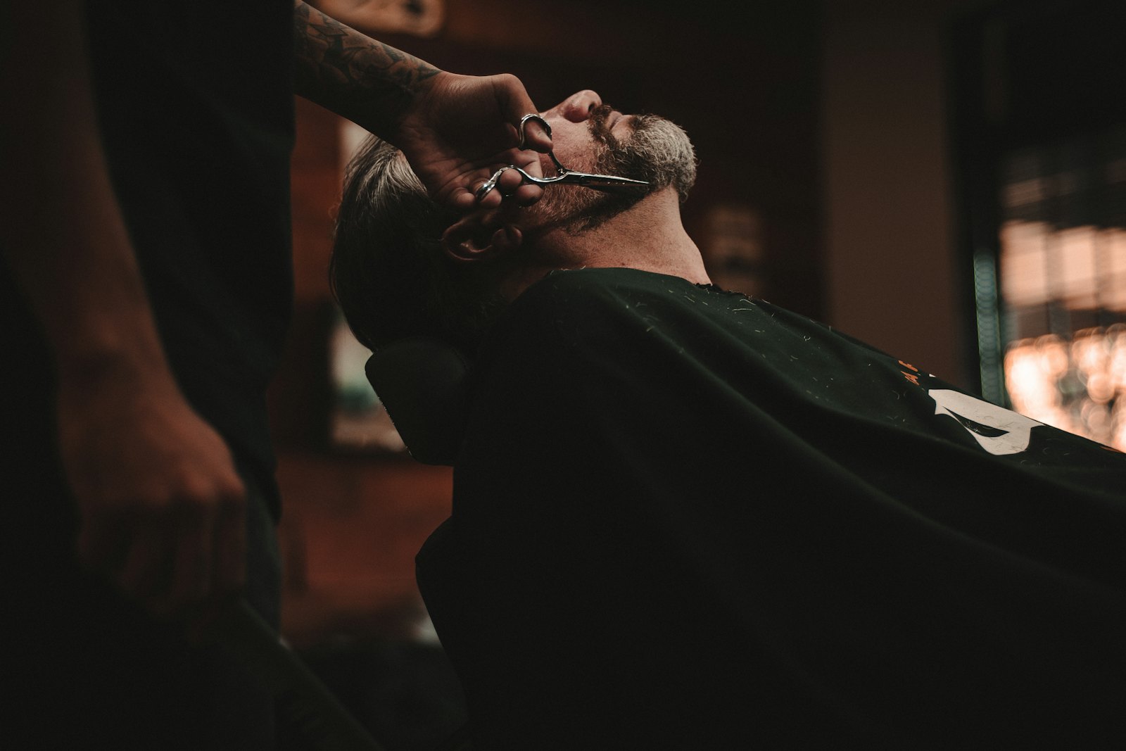 Pelanggan bersandar di kursi barber saat dicukur dengan gunting