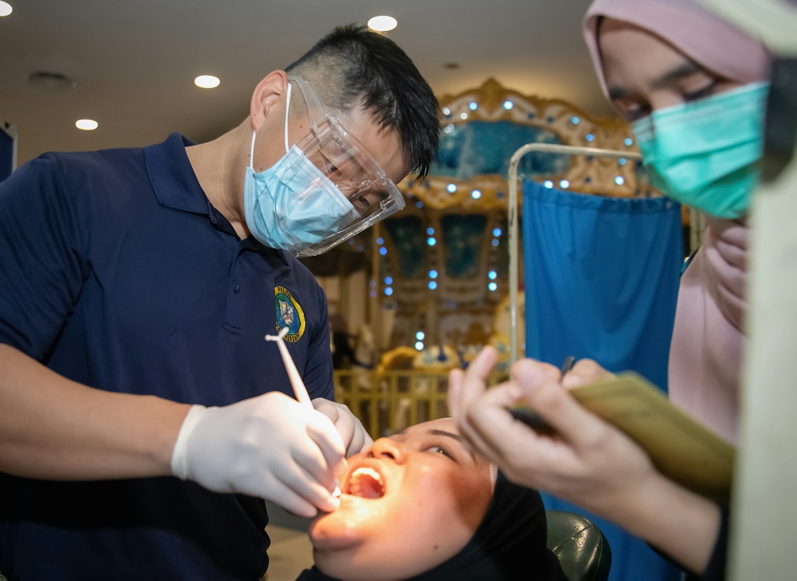 Dokter gigi bermasker dan bersarung tangan memeriksa gigi pasien